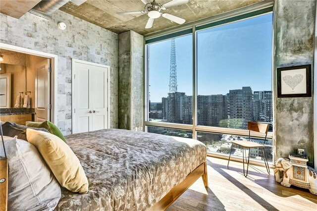 bedroom with a wall of windows, wood finished floors, a ceiling fan, and a city view