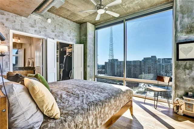 bedroom with a view of city, floor to ceiling windows, a closet, a spacious closet, and wood finished floors