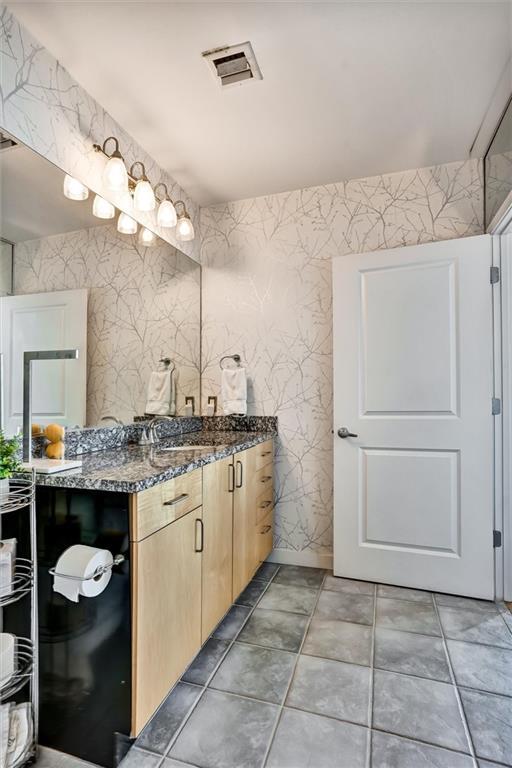 bathroom with baseboards, vanity, visible vents, and wallpapered walls