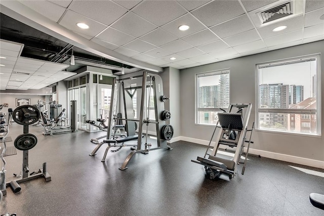 exercise room with a wealth of natural light, visible vents, a drop ceiling, and baseboards