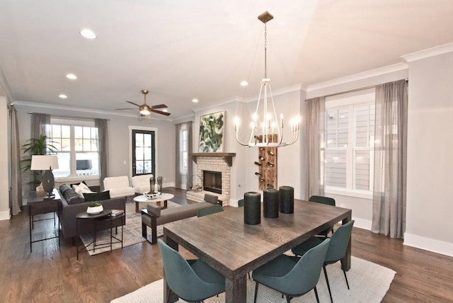 dining area featuring a brick fireplace, crown molding, ceiling fan with notable chandelier, and dark hardwood / wood-style floors