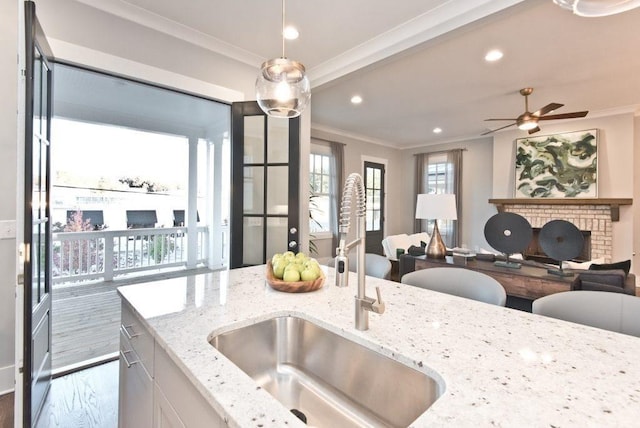 kitchen with white cabinetry, decorative light fixtures, light stone countertops, crown molding, and sink