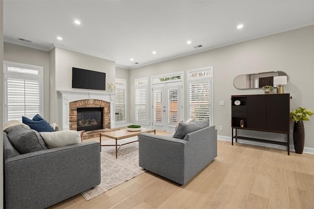 living room with french doors, light hardwood / wood-style flooring, crown molding, and a stone fireplace