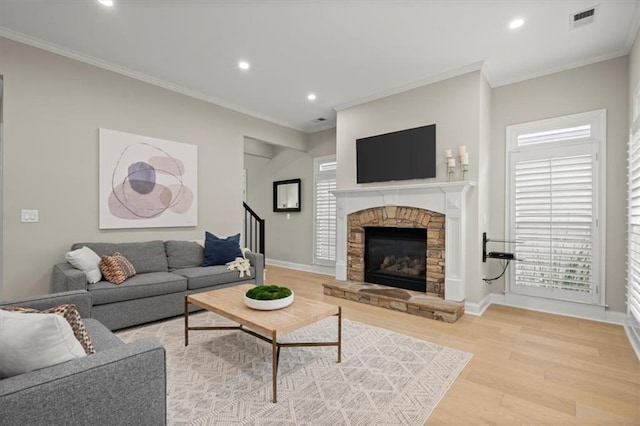 living room featuring light wood-type flooring, ornamental molding, and a fireplace