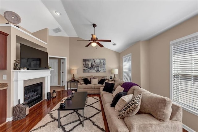 living area featuring a glass covered fireplace, lofted ceiling, wood finished floors, and visible vents