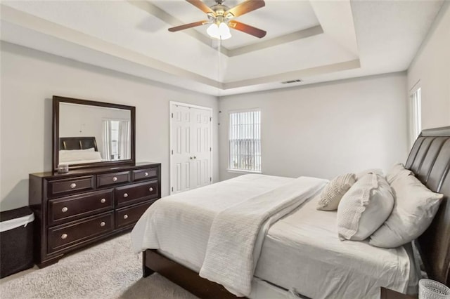 bedroom featuring visible vents, a closet, a raised ceiling, light colored carpet, and ceiling fan