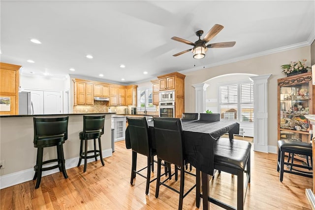 dining area with decorative columns, ceiling fan, ornamental molding, light wood-style flooring, and arched walkways