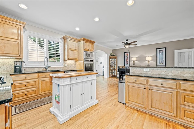 kitchen with appliances with stainless steel finishes, a sink, arched walkways, decorative backsplash, and ornamental molding