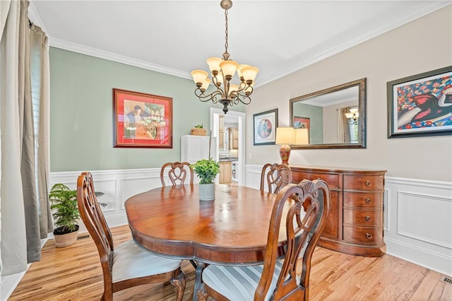 dining room with a chandelier, light wood finished floors, crown molding, a wainscoted wall, and a decorative wall