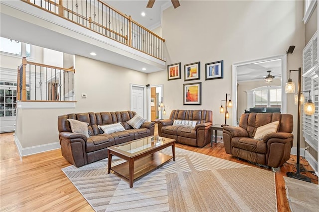 living room with ceiling fan, a towering ceiling, wood finished floors, baseboards, and a fireplace