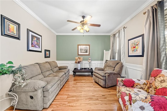 living area with crown molding, ceiling fan, light wood-style flooring, a wainscoted wall, and a decorative wall