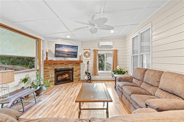 living room featuring a wall mounted air conditioner, wood finished floors, ceiling fan, a stone fireplace, and wooden walls