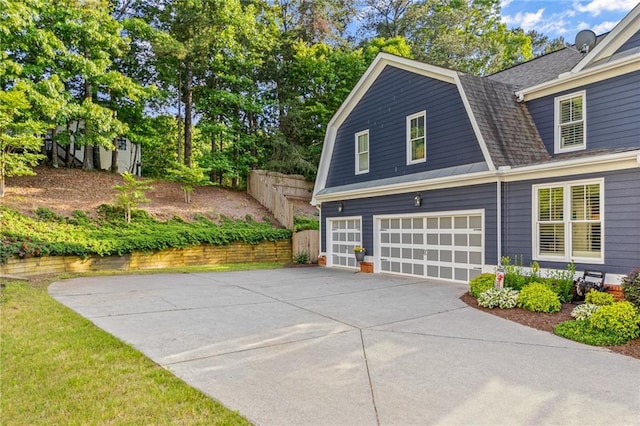 view of home's exterior featuring a gambrel roof, driveway, a garage, fence, and a shingled roof