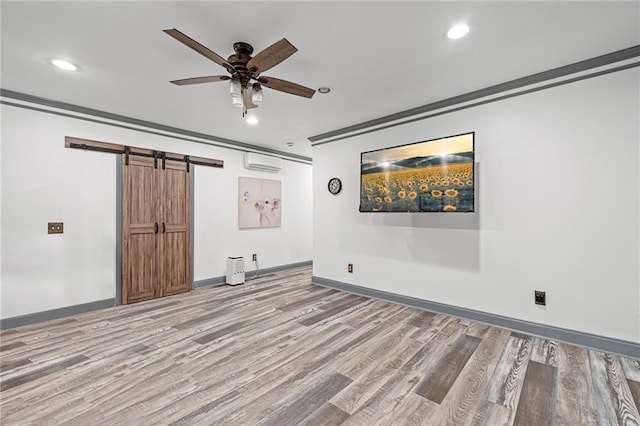 empty room with wood finished floors, ceiling fan, a barn door, an AC wall unit, and recessed lighting