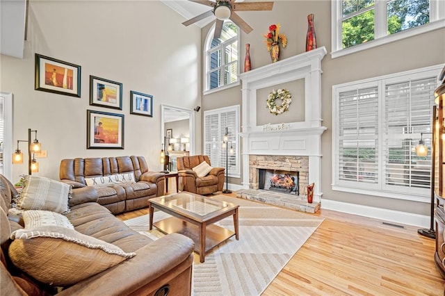 living area featuring a ceiling fan, a fireplace, a high ceiling, wood finished floors, and baseboards
