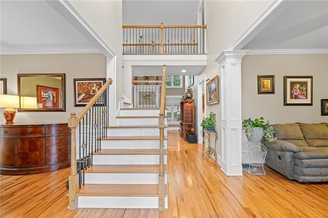 stairs with ornate columns, wood finished floors, crown molding, and a high ceiling
