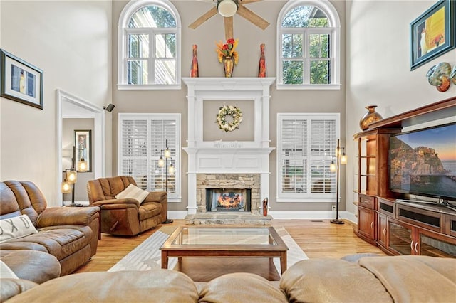 living area with a fireplace, plenty of natural light, light wood finished floors, and a towering ceiling