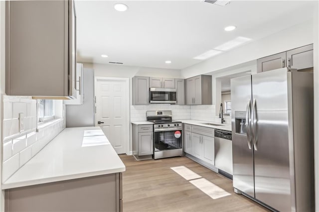 kitchen featuring decorative backsplash, appliances with stainless steel finishes, gray cabinetry, sink, and light hardwood / wood-style flooring