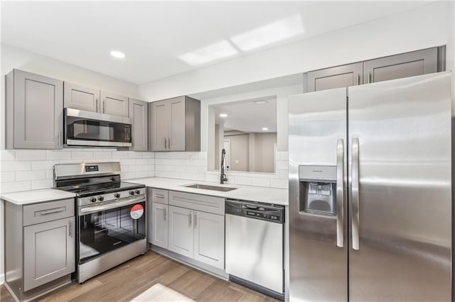 kitchen featuring appliances with stainless steel finishes, backsplash, sink, light hardwood / wood-style flooring, and gray cabinets