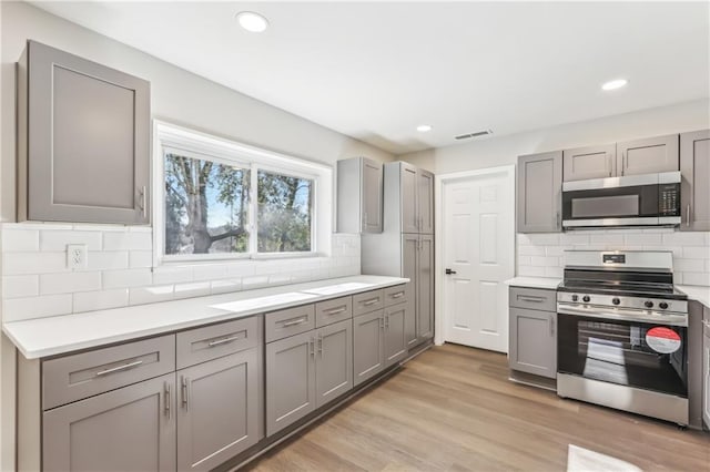 kitchen featuring backsplash, stainless steel appliances, light hardwood / wood-style flooring, and gray cabinetry