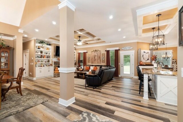 living room featuring ceiling fan, ornamental molding, coffered ceiling, light wood-type flooring, and ornate columns