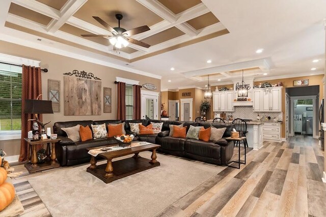 living room with ceiling fan, light wood-type flooring, ornamental molding, and coffered ceiling