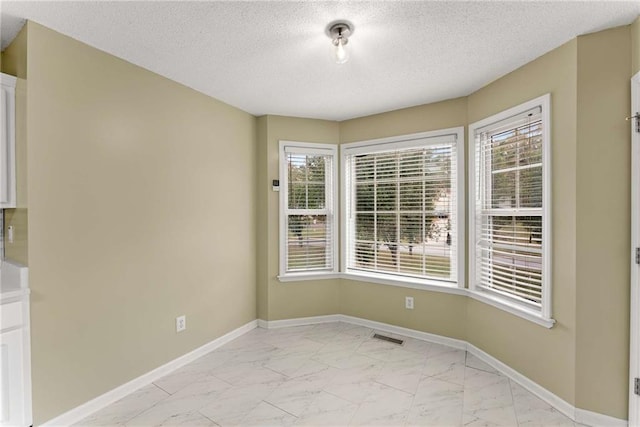 empty room with marble finish floor, baseboards, and a textured ceiling