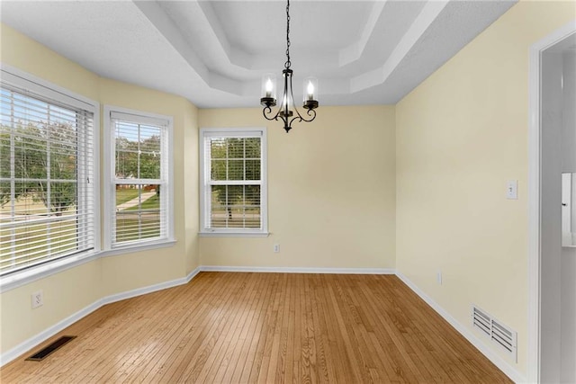 unfurnished dining area featuring a raised ceiling, visible vents, wood-type flooring, and baseboards