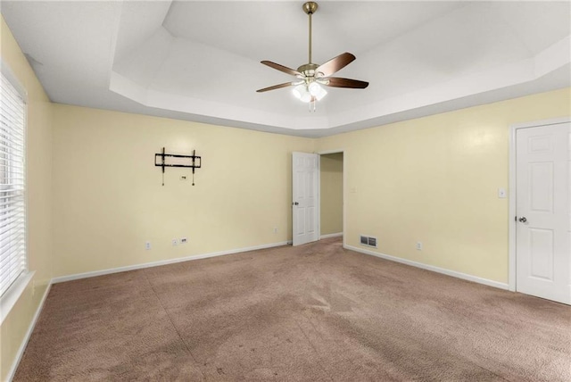 carpeted empty room featuring a ceiling fan, a tray ceiling, visible vents, and baseboards