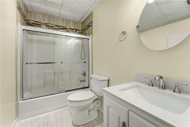 full bathroom featuring enclosed tub / shower combo, a drop ceiling, vanity, and toilet