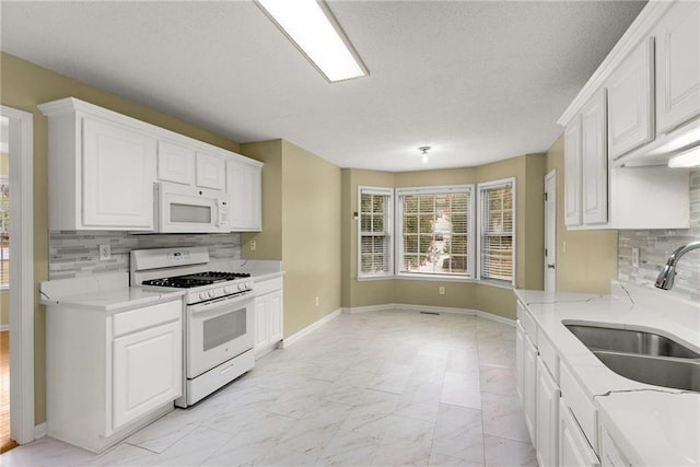 kitchen with marble finish floor, white cabinetry, a sink, white appliances, and baseboards