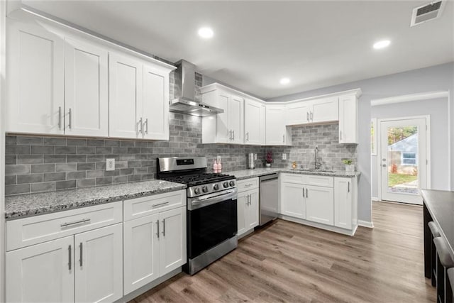1245 Meriwether St, Griffin, GA 30224 - kitchen with stainless steel appliances, wall chimney exhaust hood, white cabinetry, light wood-style floors, and a sink
