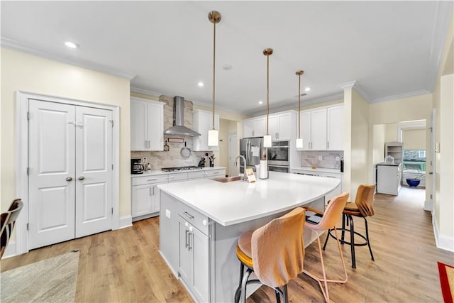 kitchen with white cabinets, a kitchen breakfast bar, a kitchen island with sink, and wall chimney exhaust hood