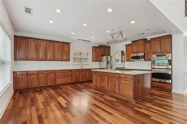4540 Hastings Dr, Cumming, GA 30041 - kitchen with appliances with stainless steel finishes, dark wood-type flooring, recessed lighting, brown cabinetry, and a center island