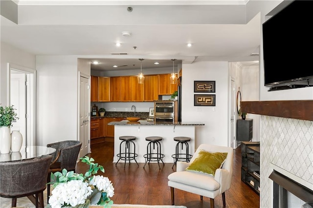 kitchen with a kitchen bar, brown cabinets, a peninsula, a fireplace, and dark wood-style flooring