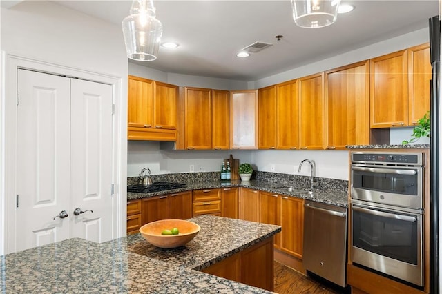 kitchen with dark stone counters, brown cabinets, appliances with stainless steel finishes, and a sink