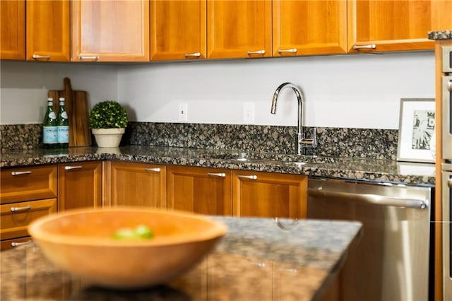 kitchen featuring dark stone counters, stainless steel dishwasher, and brown cabinetry