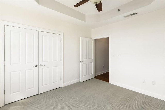 unfurnished bedroom featuring baseboards, visible vents, a closet, light carpet, and a raised ceiling