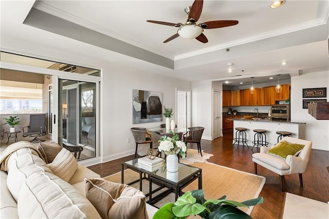 living room with baseboards, dark wood finished floors, a tray ceiling, ornamental molding, and recessed lighting