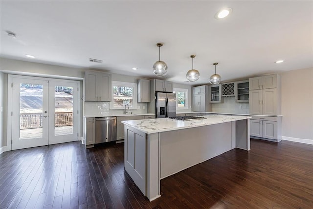 kitchen with light stone counters, dark hardwood / wood-style floors, a kitchen island, pendant lighting, and stainless steel appliances