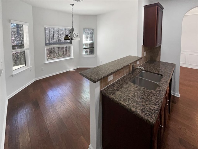 kitchen with dark stone countertops, arched walkways, dark wood-style flooring, and a sink