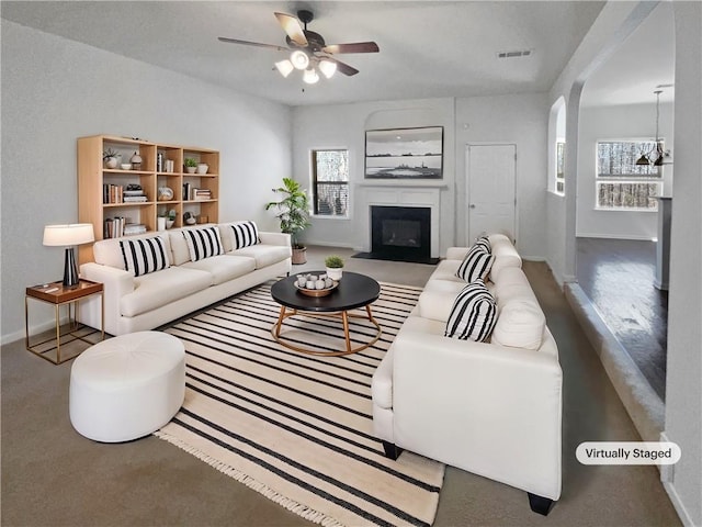 living area with visible vents, a glass covered fireplace, arched walkways, baseboards, and ceiling fan