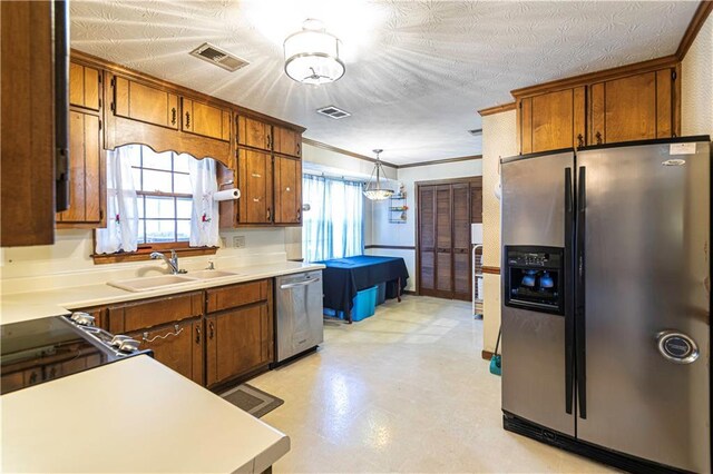 kitchen with sink, stainless steel appliances, pendant lighting, a textured ceiling, and ornamental molding