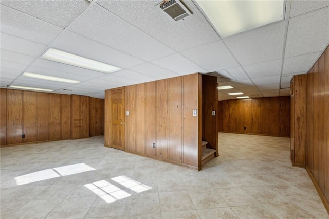 basement with a drop ceiling and wood walls