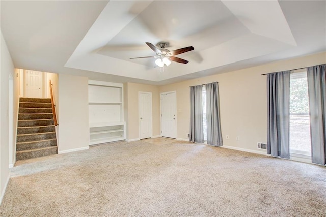 interior space with ceiling fan, light colored carpet, built in features, and a raised ceiling