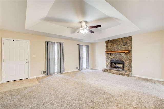 unfurnished living room featuring ceiling fan, a tray ceiling, light carpet, and a stone fireplace