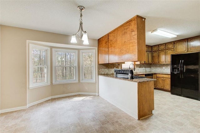 kitchen featuring black fridge, kitchen peninsula, dark stone counters, hanging light fixtures, and a notable chandelier