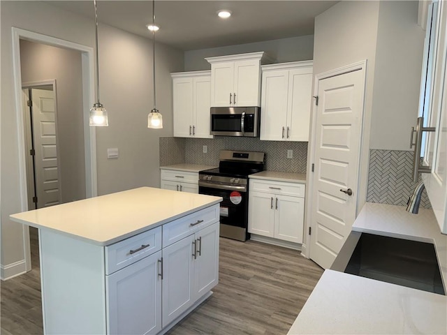 kitchen with white cabinetry, tasteful backsplash, light hardwood / wood-style floors, decorative light fixtures, and appliances with stainless steel finishes