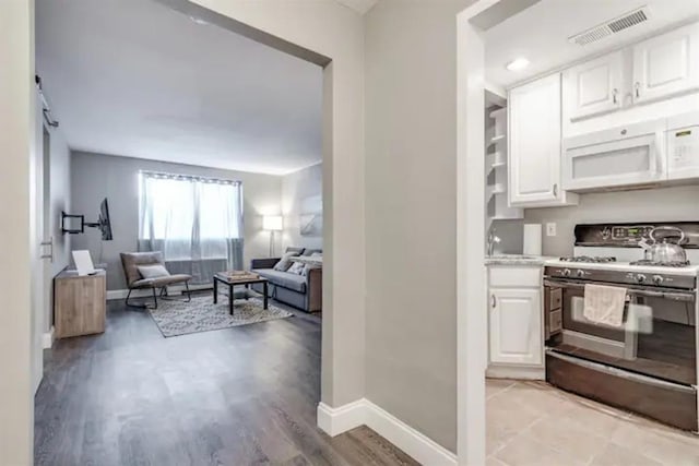 kitchen featuring visible vents, range with gas stovetop, white cabinetry, open floor plan, and white microwave