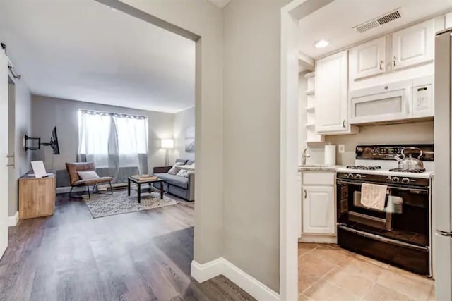 kitchen featuring gas range, baseboards, visible vents, white cabinets, and white microwave